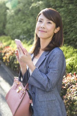 Parkta akıllı telefon kullanan Asyalı kadın. 