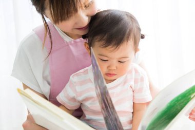 Asyalı anaokulu öğretmeni ve odada kitap okuyan sevimli küçük kız.