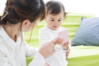 Asyalı kadın sevimli küçük kızıyla birlikte cep telefonu kullanıyor..