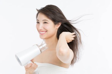 Gülümseyen Asyalı kadın beyaz arka planda saçlarını kurutan.