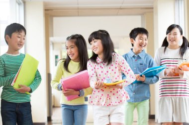 Okul koridorunda yürüyen kitaplarla bir grup Japon çocuk. 