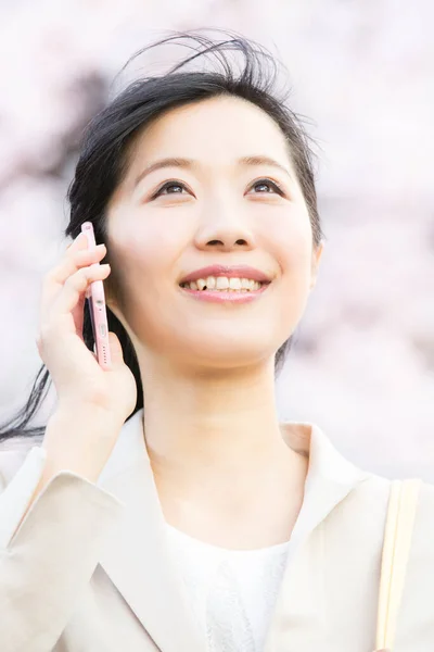 美丽的年轻亚洲女人用智能手机说话 抬头看着春天的公园 — 图库照片