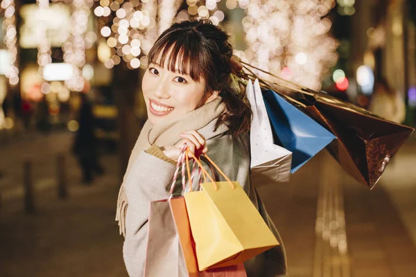 身穿秋装的日本美女站在街上 提着购物袋 点亮了城市的背景 — 图库照片