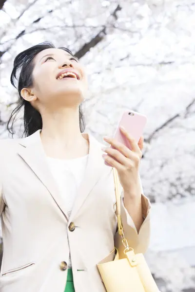 美丽的年轻亚洲女人用智能手机抬头看春天的公园 — 图库照片