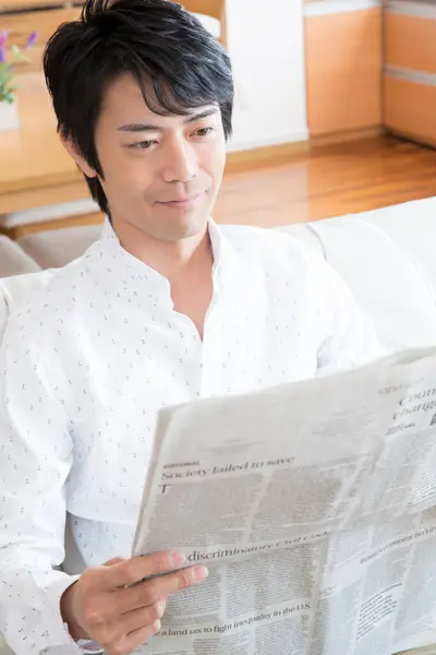 asian man reading a newspaper on the sofa