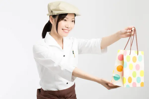 Portret Uśmiechniętej Azjatyckiej Kelnerki Trzymającej Kolorowy Worek Wyciągniętych Ramionach — Zdjęcie stockowe
