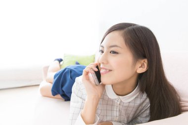 Kanepede cep telefonu kullanan Asyalı kadın. 