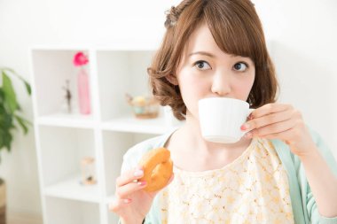 Genç bir kadın kahve içiyor ve kahvaltı yapıyor.