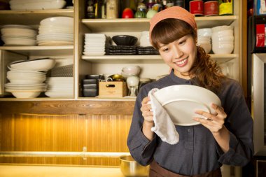 Asyalı garson kadın tabak siliyor.