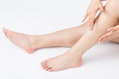 Genç bir kadın beyaz arka planda krem sürüyor.