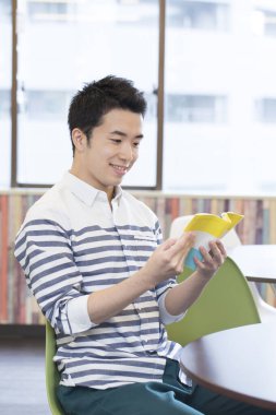 Asyalı öğrenci üniversitede masada okuyor. 