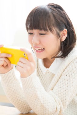 Oturma odasında akıllı telefon kullanan Asyalı kadın.