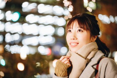 Sonbahar elbiseli güzel Japon kadın sokakta oturuyor, aydınlanmış şehir arka planında. 