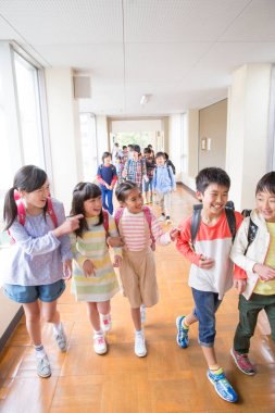Okul koridorunda sırt çantalı bir grup Japon çocuk yürüyor. 