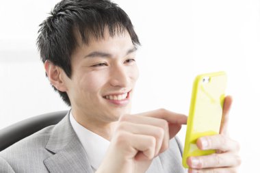 Genç Asyalı işadamı ofiste akıllı telefon kullanıyor.