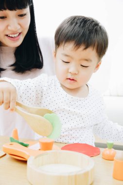 Asyalı anne ve oğlu evde tahta oyuncaklarla oynuyorlar. 
