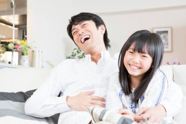 Genç Asyalı baba ve kızı kanepede gülüyor.