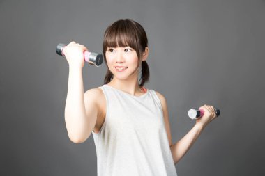 Asyalı kadın spor salonunda dambıllarla egzersiz yapıyor.