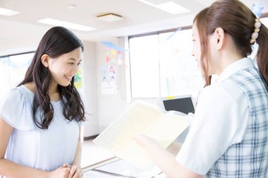 Ehliyet kursunda danışmanıyla konuşan Asyalı genç bir kadının portresi.