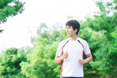 Genç yakışıklı Asyalı adam parkta koşuyor. 