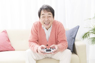 Asyalı yaşlı adam evde video oyunu oynuyor.