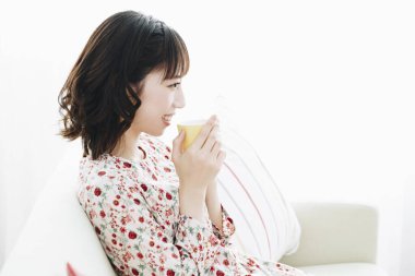 Asyalı genç kadın evdeki yatak odasında çay içiyor..