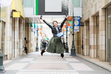 Siyah ceketli genç bir kadın şehrin arka planında zıplıyor.