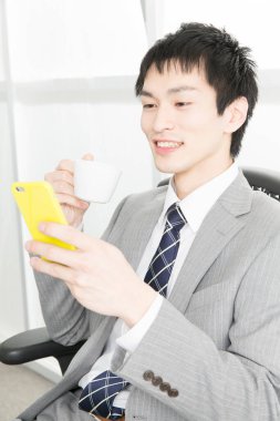 İş adamı elinde bir fincan kahveyle akıllı telefon kullanıyor. 