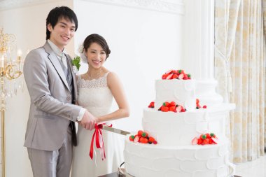 Mutlu genç Japon gelin ve damat düğün pastasını kesiyor.