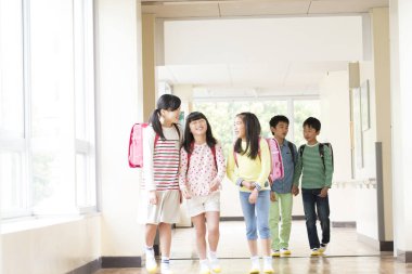 Okul koridorunda sırt çantalı bir grup Japon çocuk yürüyor. 