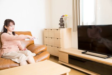 Genç Asyalı kadın evde televizyon izliyor.