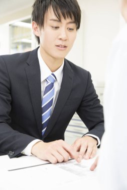 Genç Asyalı işadamı ofiste müşteriyle birlikte çalışıyor.