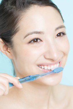 Genç kadın mavi arka plan üzerinde diş fırçalama 