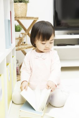 Küçük kız yerde kitap okuyor. 