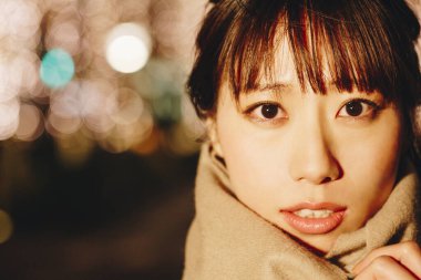 Sonbahar elbiseli güzel Japon kadın sokakta oturuyor, aydınlanmış şehir arka planında. 