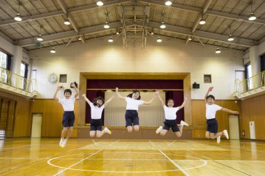 Okulun jimnastik salonunda atlayan Asyalı öğrenciler. 