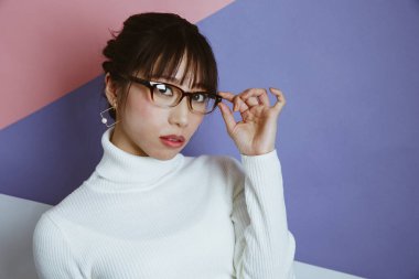 Gözlüklü genç Asyalı kadın stüdyoda poz veriyor.