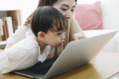 Asyalı anne ve küçük kızı evde dizüstü bilgisayar kullanıyorlar.