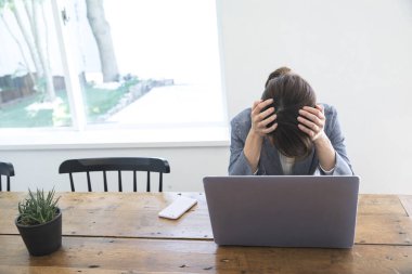 Ofis masasında dizüstü bilgisayarla oturan stresli genç kadın.