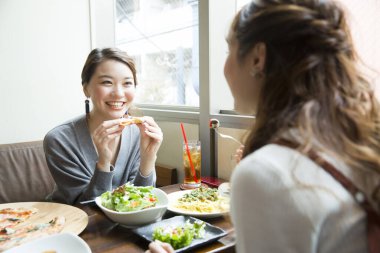 Kahvede yemek yiyen gülümseyen Japon kadınlar.