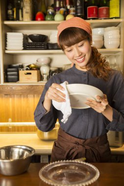 Asyalı garson kadın tabak siliyor.