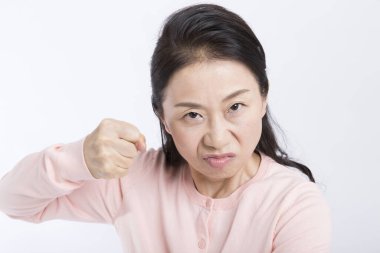 Asyalı kızgın yaşlı kadın beyaz arka planda yumruğunu gösteriyor.