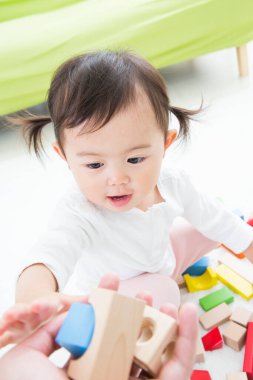 Anaokulunun zemininde renkli oyuncak bloklarıyla oynayan Asyalı çocuk.
