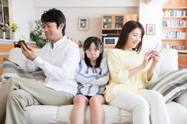 Ailesi kanepede akıllı telefon kullanan üzgün Asyalı kız. 