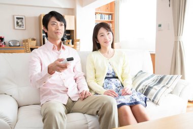 Asyalı çift oturma odasında televizyon izliyor. 