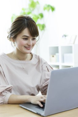 Genç Asyalı kadın evde dizüstü bilgisayar kullanıyor.