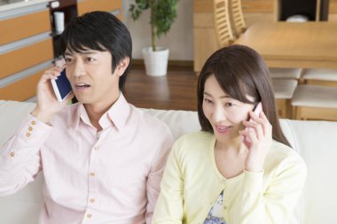 Genç Asyalı çift akıllı telefonlarıyla kanepede oturuyor.