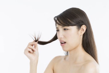 Asyalı kadın uzun saçlarını tutuyor ve hasarlı saç uçlarına bakıyor. 