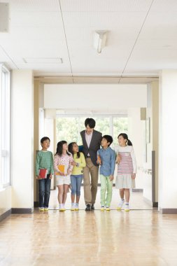 Öğretmenli bir grup Japon çocuk okul koridorunda yürüyor. 