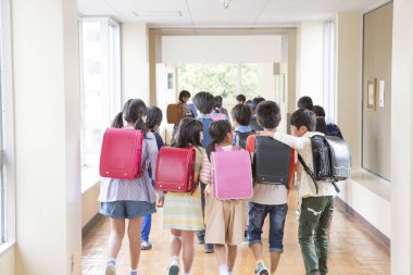 Okul koridorunda sırt çantalı bir grup Japon çocuk yürüyor. Arka plan